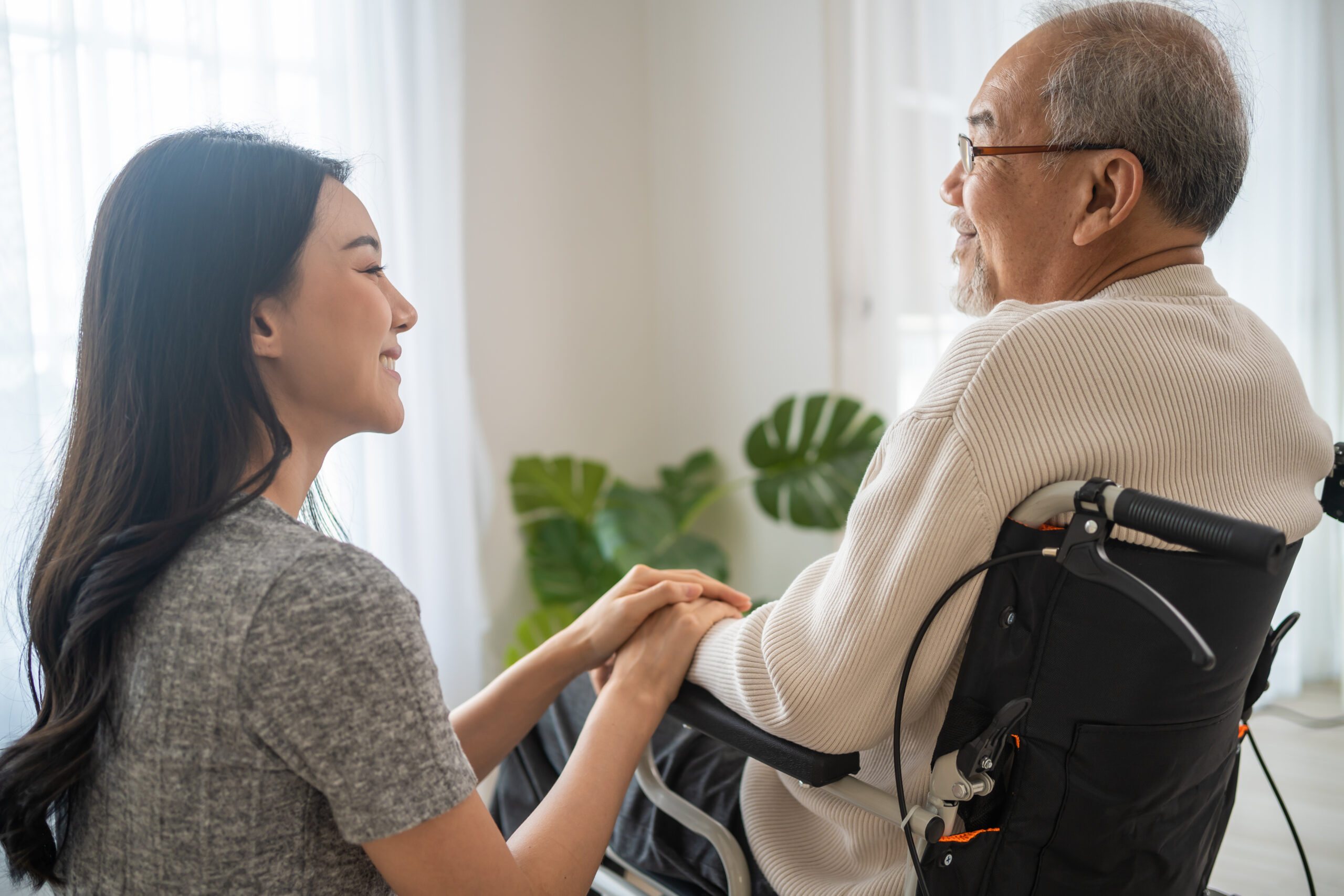 Asian daughter support old disabled man sitting on wheelchair at home. Beautiful girl help and take care of senior elderly mature handicap father patient doing physical therapy in living room in house